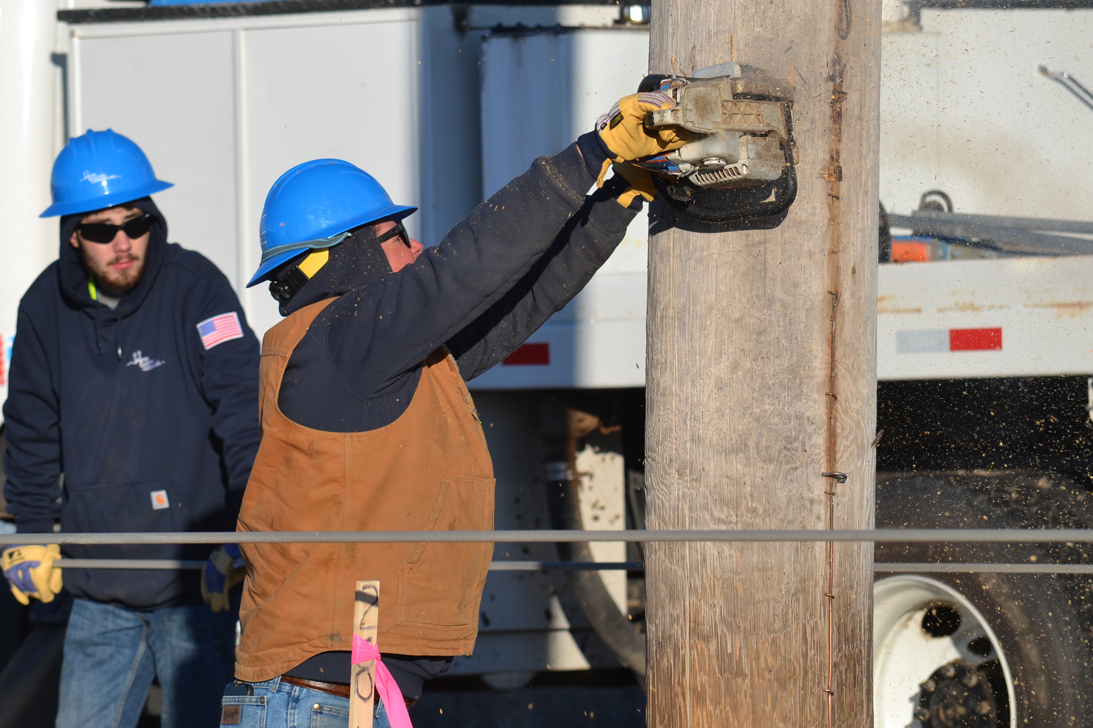 Linemen from Ward Electric cut through a pole with a chainsaw