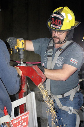 A Larned fireman uses a brushless, cordless drill to lower the grain level inside of the rescue tube. Grain spills out from a red chute.