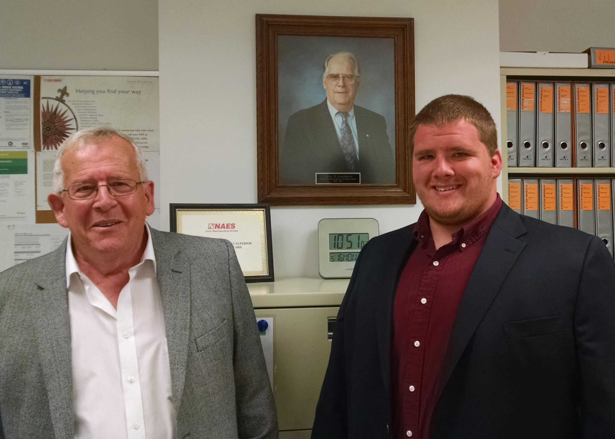 Marc Goodman and his son, Daniel Goodman, stand in front of a portrait of Jack Goodman, former president and general manager at Midwest Energy and for whom the Goodman Energy Center is named.  Jack Goodman is Marc's father and Daniel's grandfather.