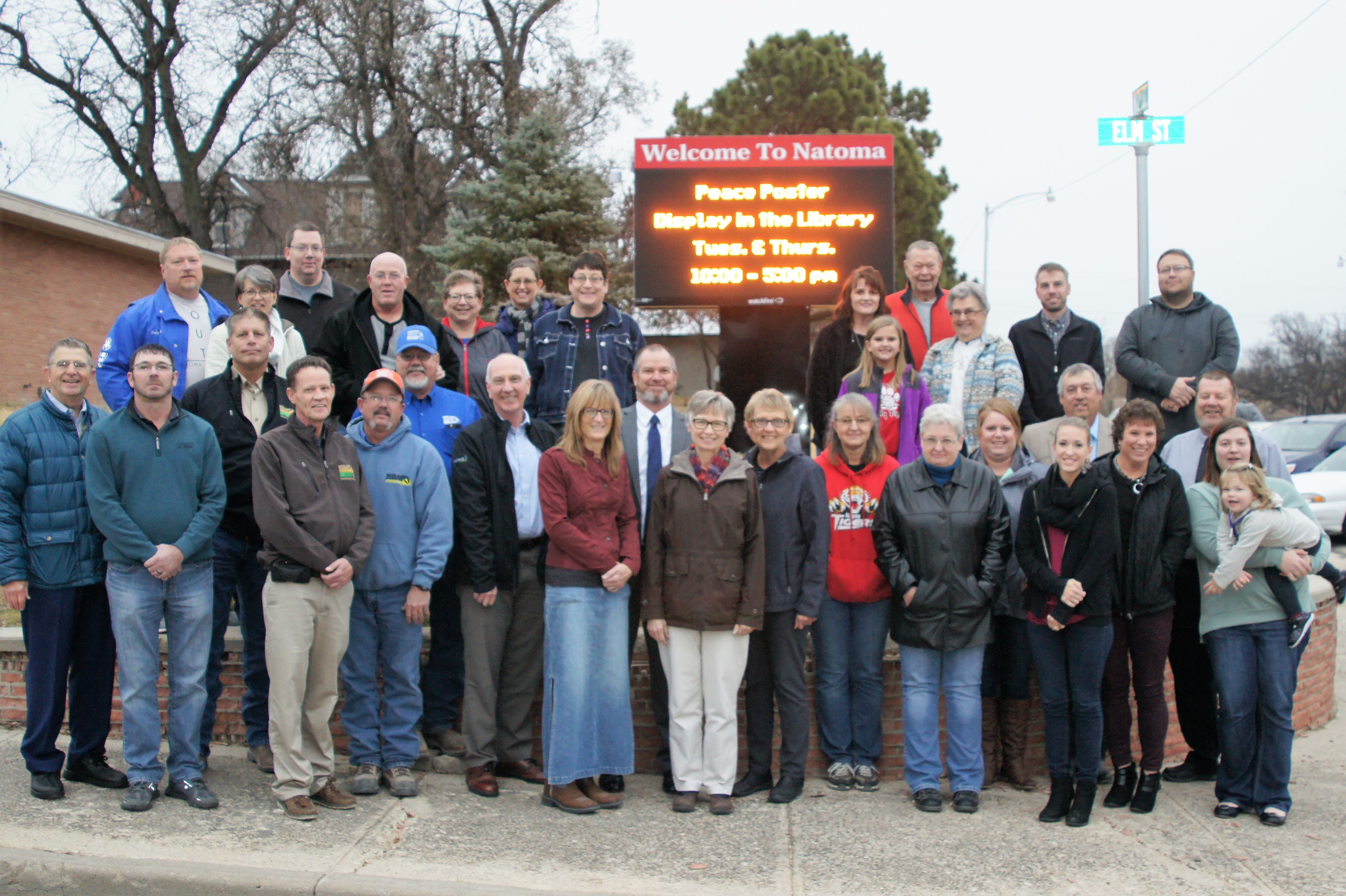 More than two dozen citizens of Natoma, Kansas stand in front of a large outdoor LED sign installed in the city to keep members informed of community events.
