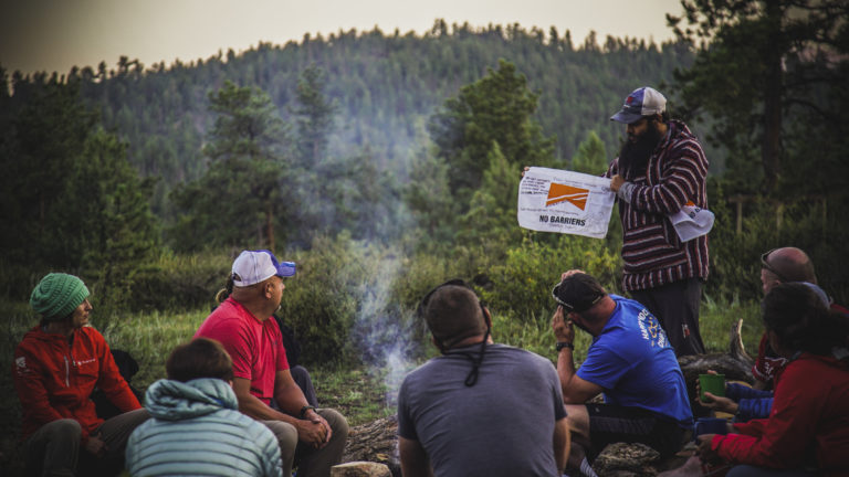 A group of veterans participating in the No Barriers Warriors program sit and talk around a campfire in the mountains near Red Feather Lakes, Colorado.