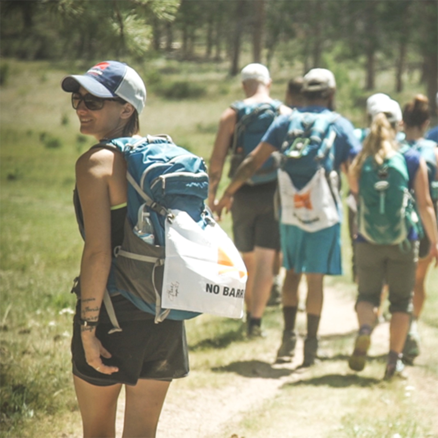 A group of veterans participating in the No Barriers Warriors program hike in the mountains near Red Feather Lakes, Colorado. A female participant is turning to face the camera as others walk ahead.