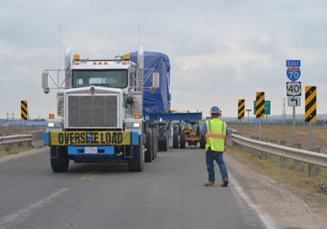 A natural gas generator, weighing 150 tons, is transported over I-70 via Bypass 183 just northwest of Hays. A white semi-truck pulls the massive generator with 130-foot specialized trailer. The trailer is mounted with several outriggers to displace the weight of the generator. Each outrigger can displace 20-tons of weight. The generator is covered with a blue tarp.