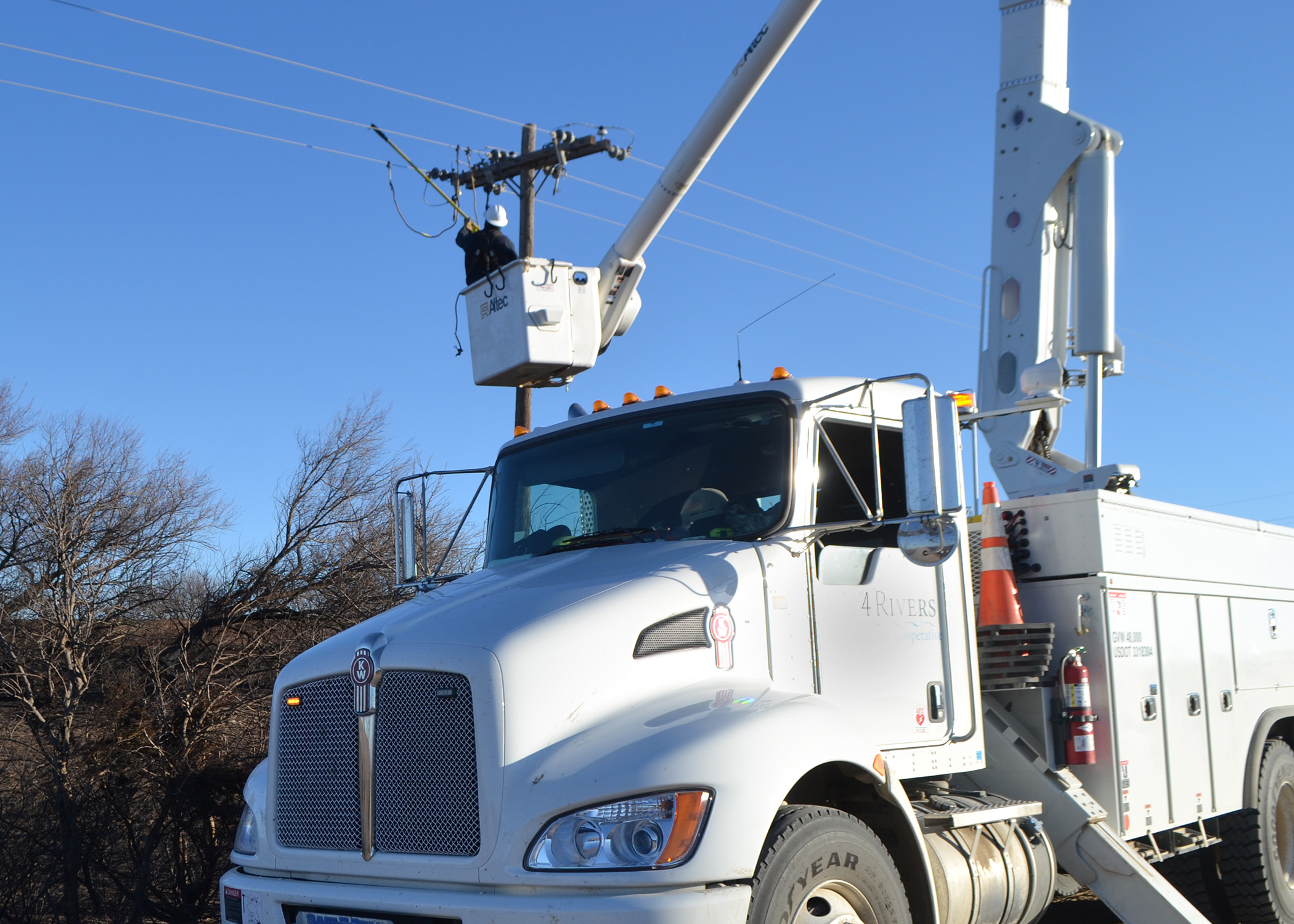 A picture of a lineman working on a power line from a white bucket truck.