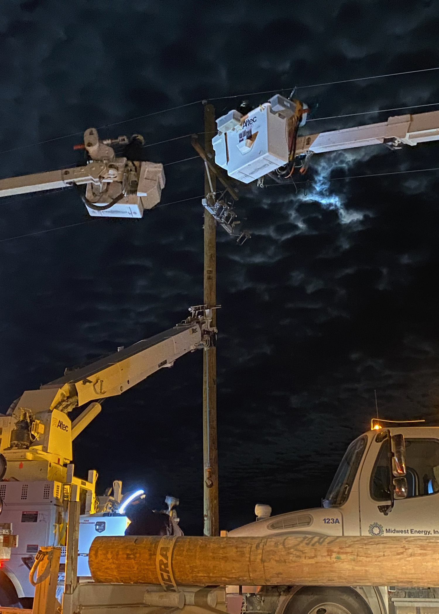 A picture of linemen in two bucket trucks working on a power pole at night.