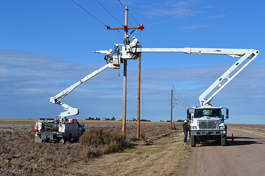 A photo of two bucket trucks, with booms extended, as linemen work on overhead power lines.