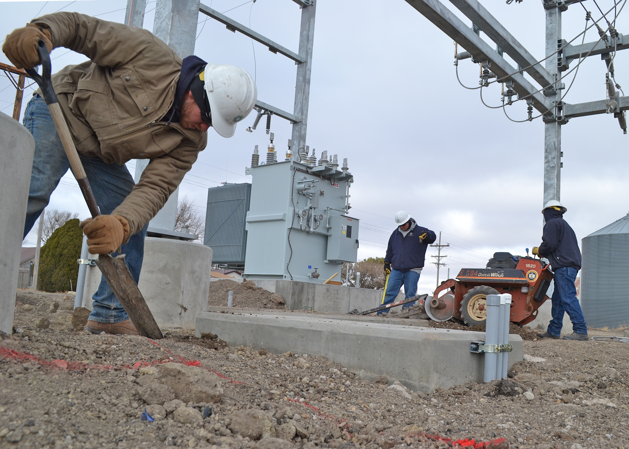 A photo of Midwest Energy linemen shoveling a trench, and operating a trenching machine, inside a new substation in Winona, Kansas.