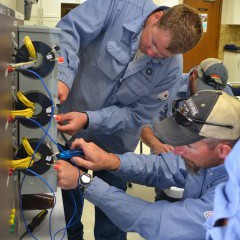 A picture of two Midwest Energy linemen in blue shirts work on a metering can simulator.