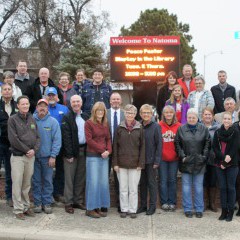 More than two dozen citizens of Natoma, Kansas stand in front of a large outdoor LED sign installed in the city to keep members informed of community events.  