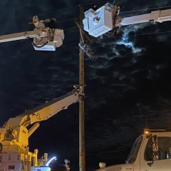 A picture of linemen in two bucket trucks working on a power pole at night.  