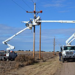 A photo of two bucket trucks, with booms extended, as linemen work on overhead power lines.