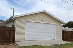 Picture of a detached two-car garage with yellow siding, behind a home.