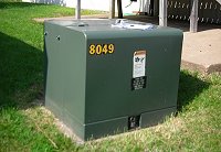 A green padmount transformer box, shown in the backyard of a home.  