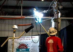 A lineman in a red shirt uses a fiberglass stick to create an arc during a high-voltage power demonstration.