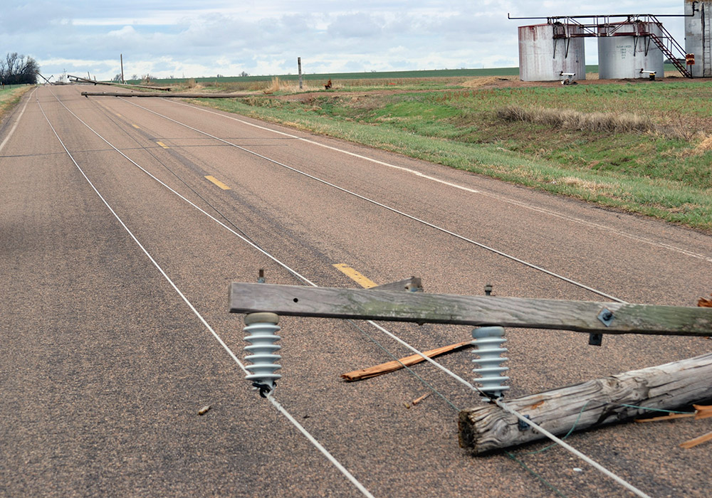 Power lines and poles lay across a rural road after a storm near Chase, Kansas.